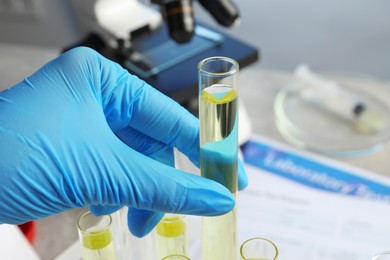 Photo of Doctor taking test tube with urine sample for analysis at table, closeup