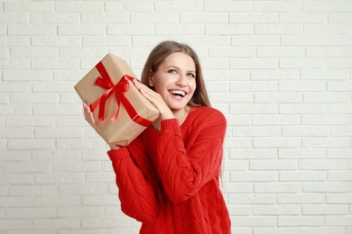 Photo of Happy young woman with Christmas gift near white brick wall