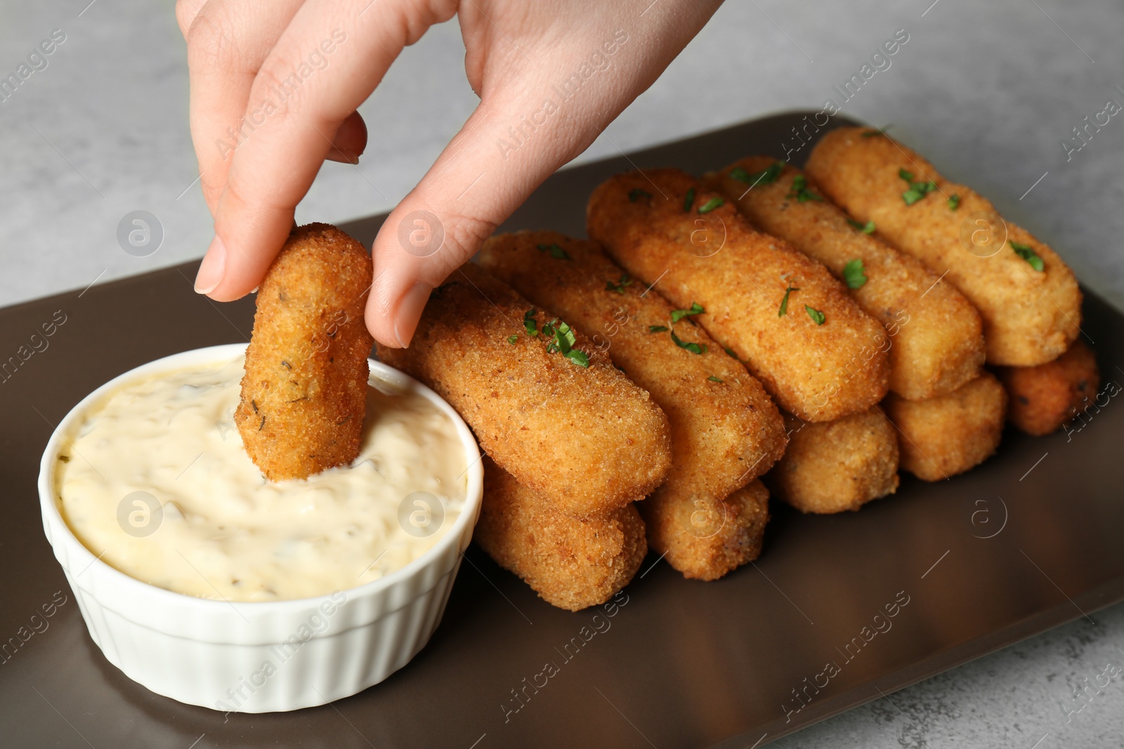 Photo of Woman dipping cheese stick into sauce at table, closeup