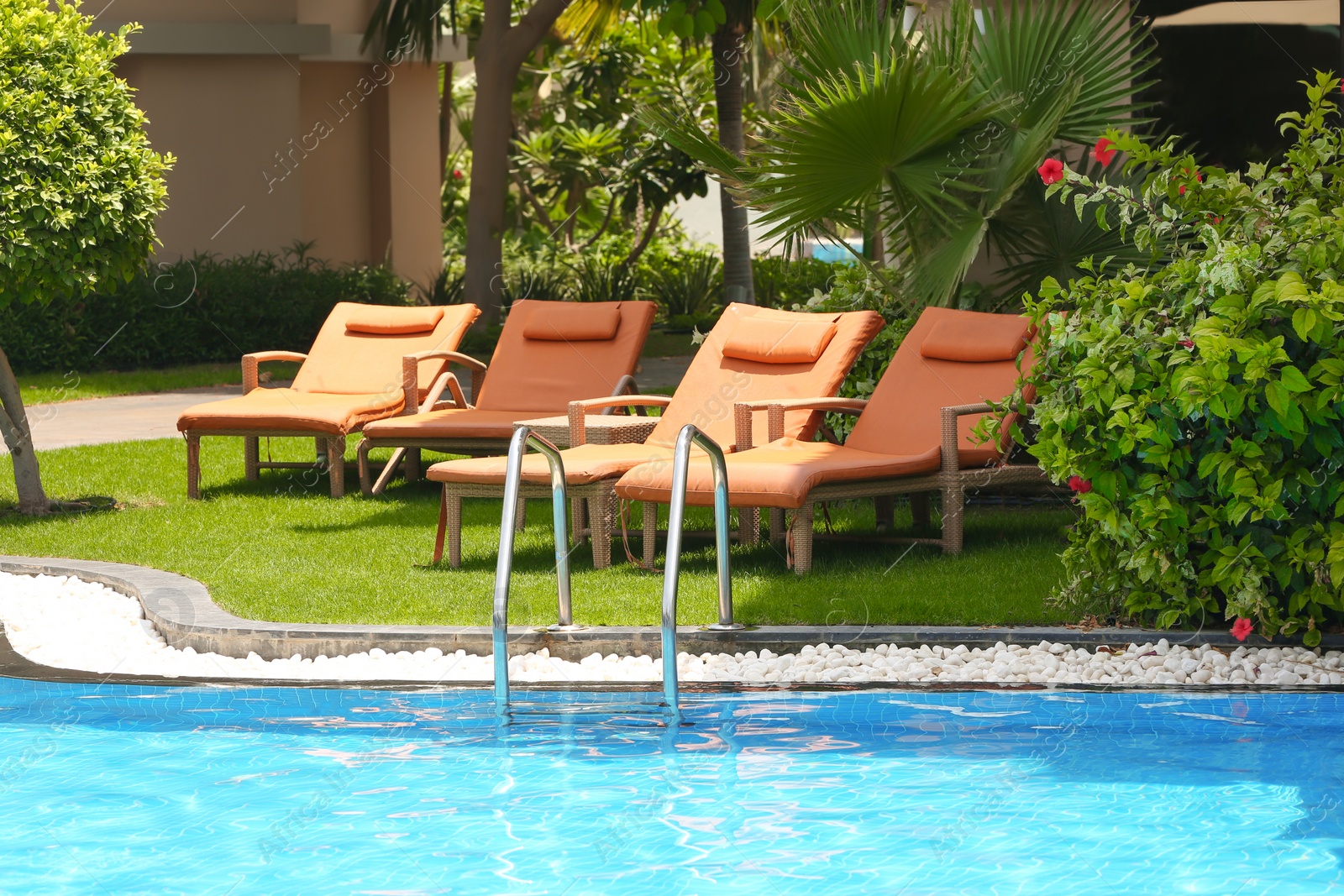 Photo of Sunbeds near modern swimming pool at resort