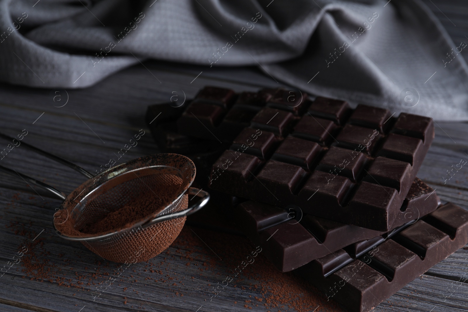 Photo of Tasty dark chocolate bars and sieve with cocoa powder on wooden table