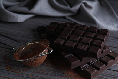 Photo of Tasty dark chocolate bars and sieve with cocoa powder on wooden table