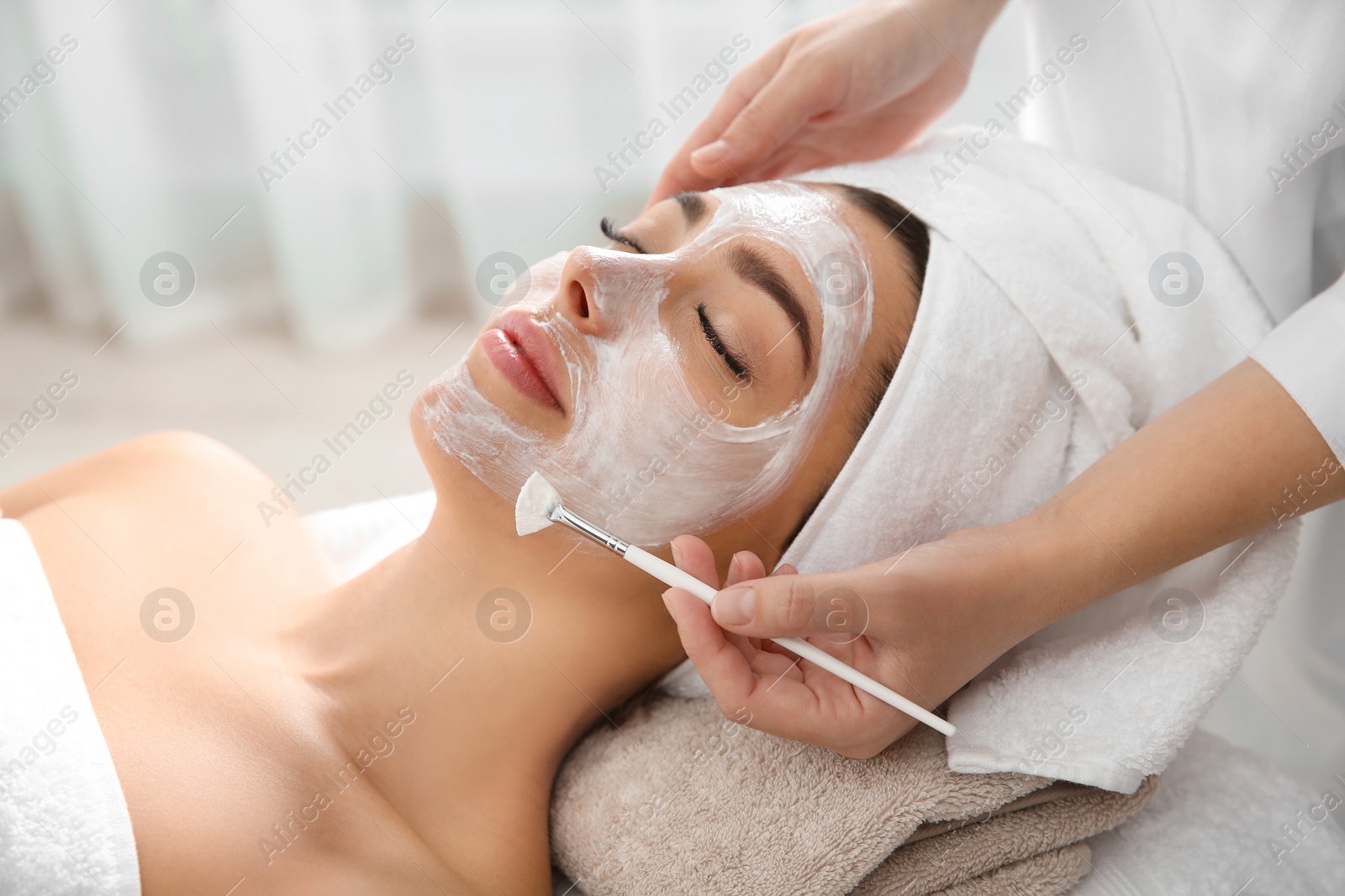 Photo of Cosmetologist applying mask on client's face in spa salon