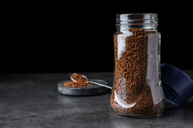 Photo of Glass jar and spoon of instant coffee on grey table against black background. Space for text