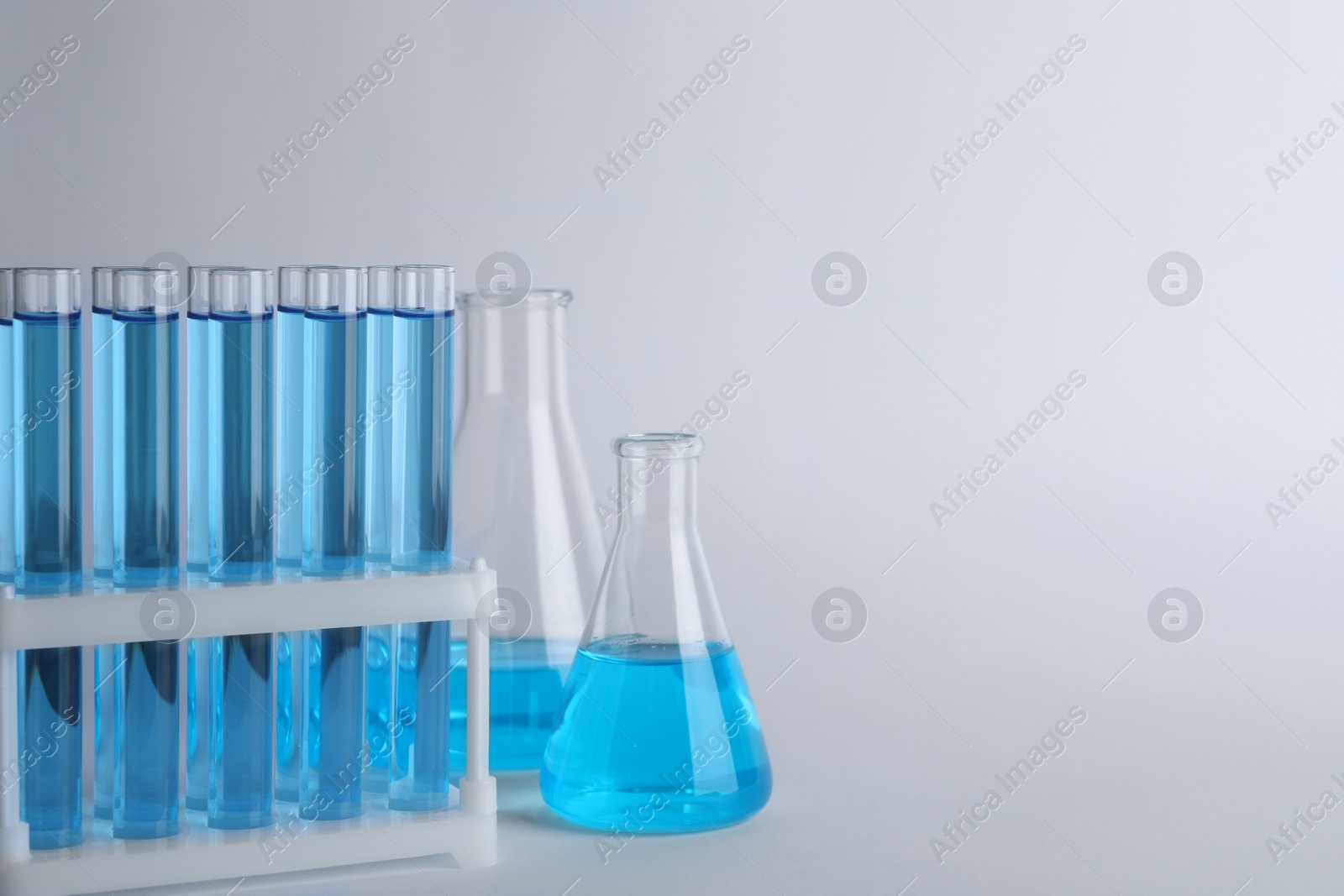 Photo of Laboratory glassware with blue liquid on light grey background. Space for text