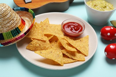 Nachos chips, sauce, Mexican sombrero hat, maracas and guacamole on light blue background