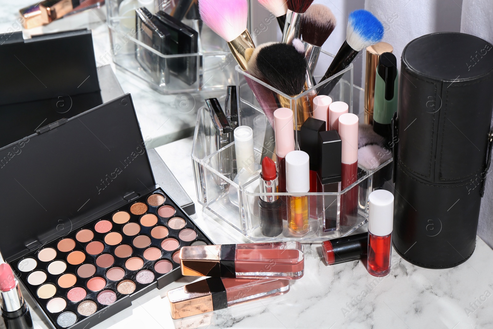 Photo of Bright lip glosses among different cosmetic products on white dressing table