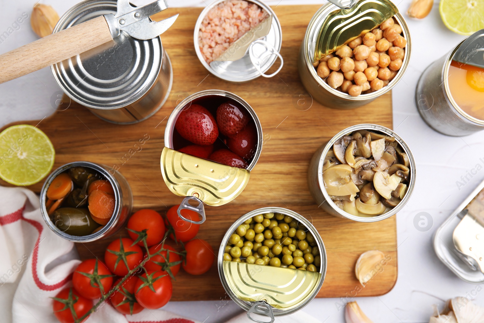 Photo of Open tin cans with different preserved products on white textured table, flat lay