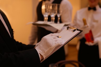 Photo of Man with clipboard teaching trainees indoors, closeup. Professional butler courses