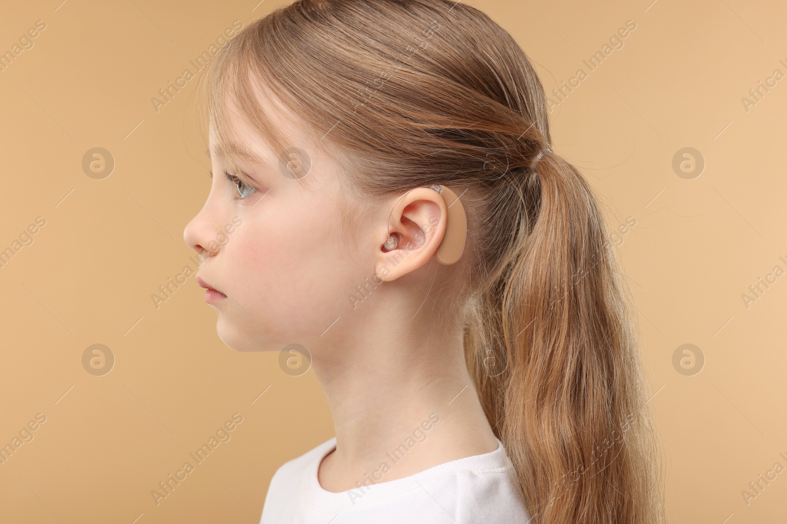 Photo of Little girl with hearing aid on pale brown background