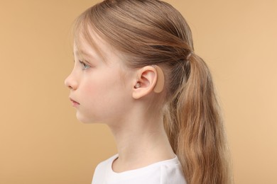 Little girl with hearing aid on pale brown background