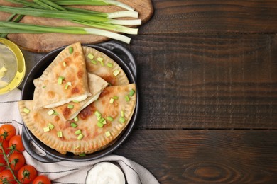 Photo of Delicious fried chebureki with cheese, green onion and ingredients on wooden table, flat lay. Space for text