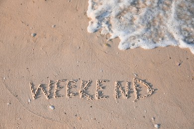 Word Weekend written on sand at beach, above view