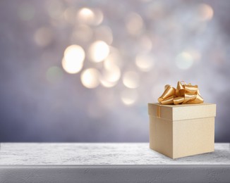 Beautiful gift box on stone table against blurred festive lights, bokeh effect. Space for text