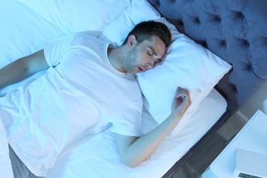 Photo of Young man sleeping in bed at night, top view