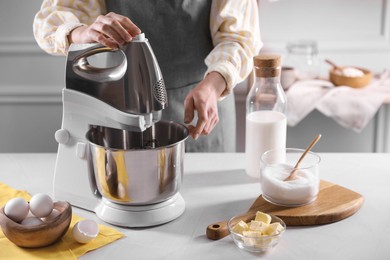 Photo of Woman making dough with stand mixer at table, closeup