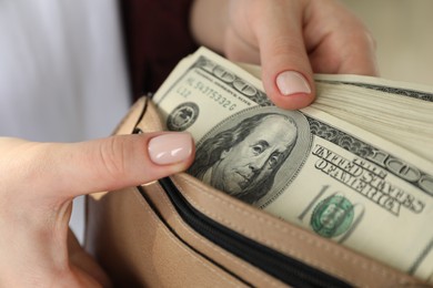 Photo of Money exchange. Woman putting dollar banknotes into wallet on blurred background, closeup