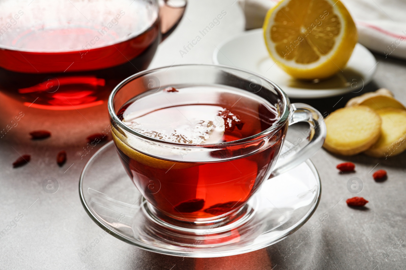 Photo of Glass cup of healthy goji tea with lemon on grey table