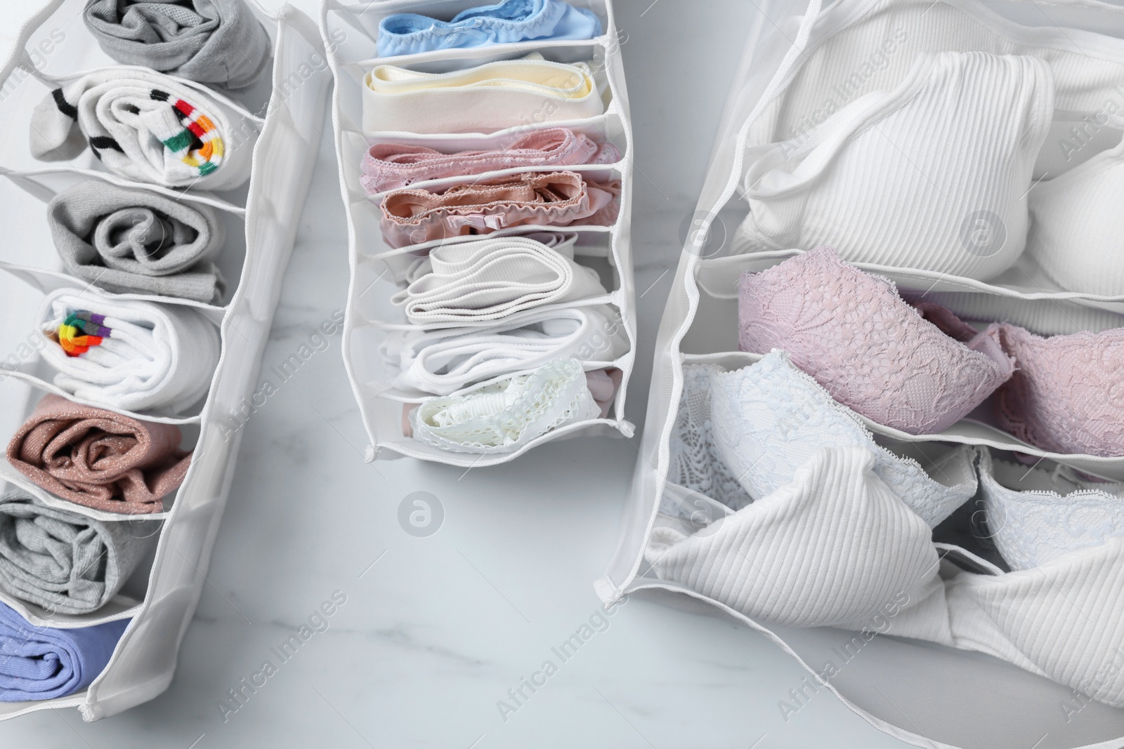 Photo of Organizers with folded women's underwear on white marble table, flat lay