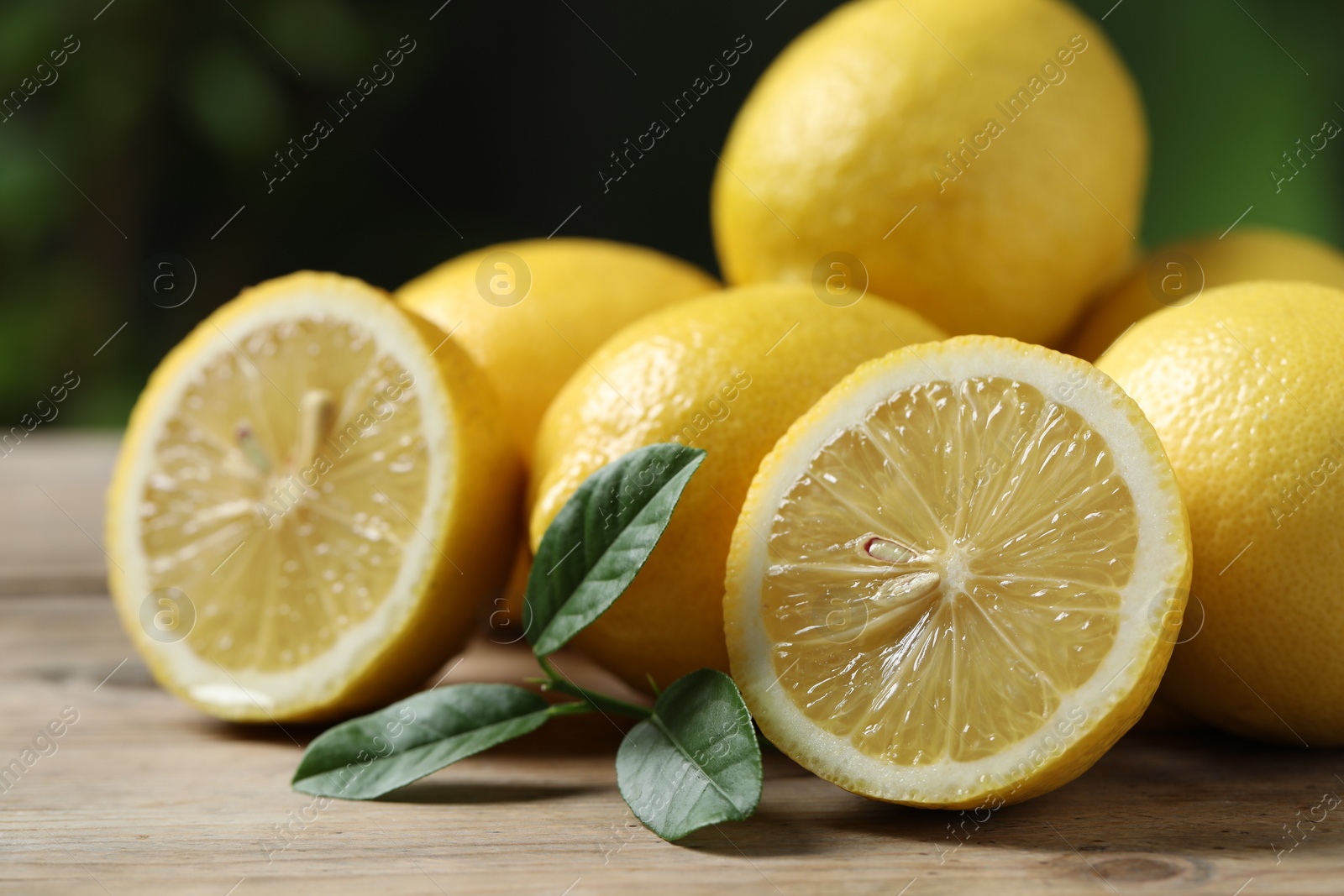 Photo of Fresh lemons and green leaves on wooden table, closeup