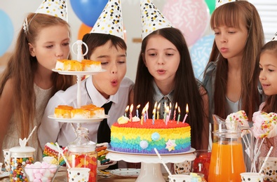 Happy children blowing out candles on cake at birthday party indoors