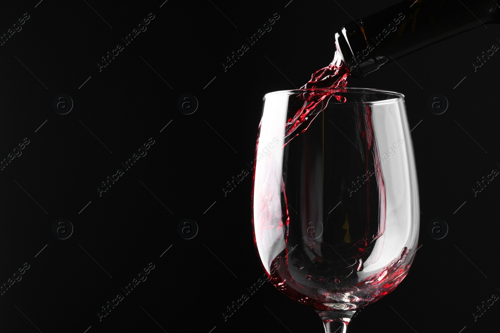 Photo of Pouring red wine into glass against black background, closeup. Space for text