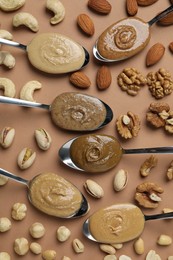 Photo of Tasty nut butters in spoons and raw nuts on light brown table, flat lay