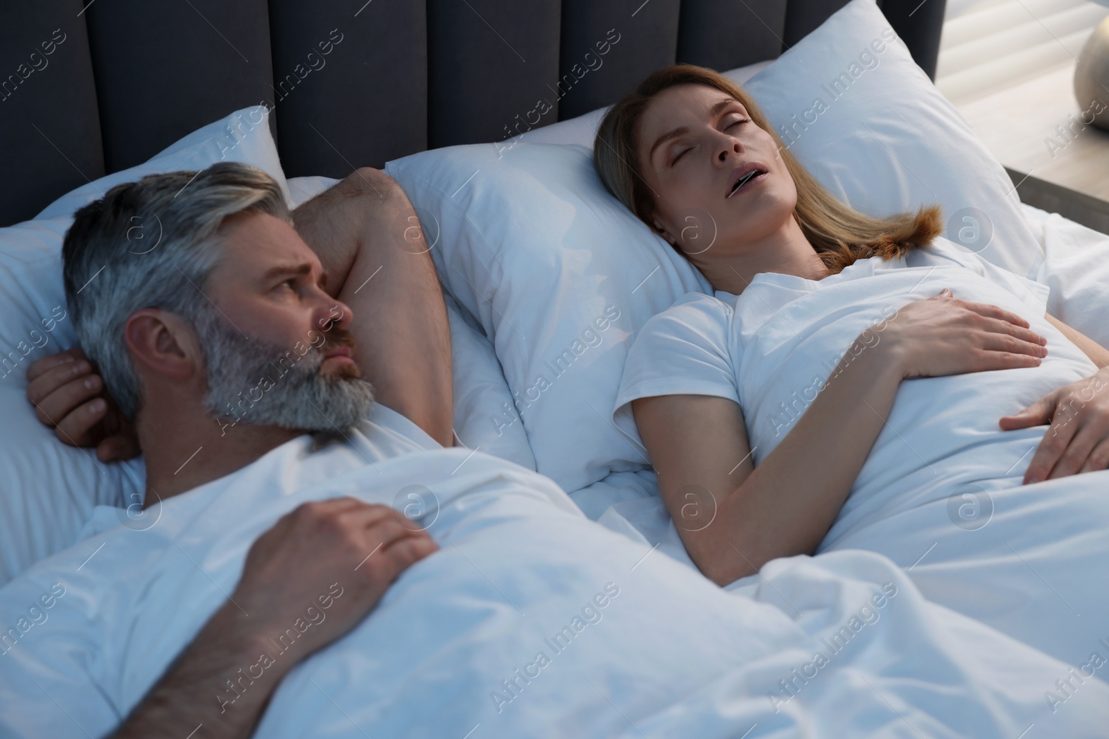 Photo of Irritated man lying near his snoring wife in bed at home