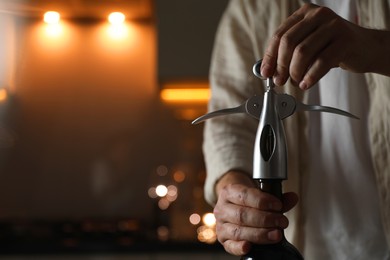 Man opening wine bottle with corkscrew on blurred background, closeup. Space for text