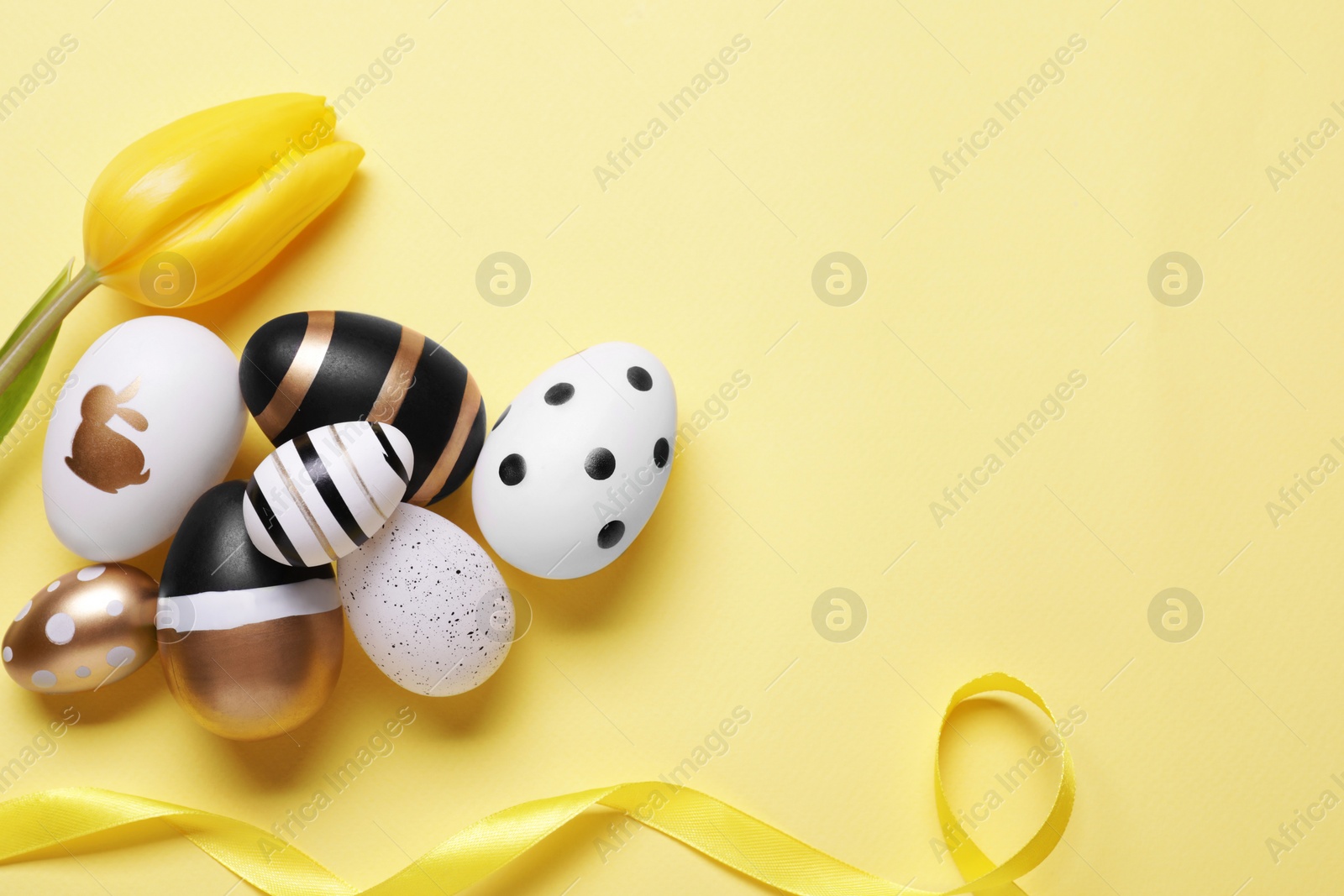 Photo of Flat lay composition with tulip and beautifully painted eggs on yellow background, space for text. Easter celebration