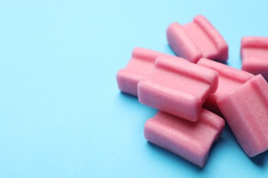 Photo of Tasty pink chewing gums on light blue background, closeup. Space for text