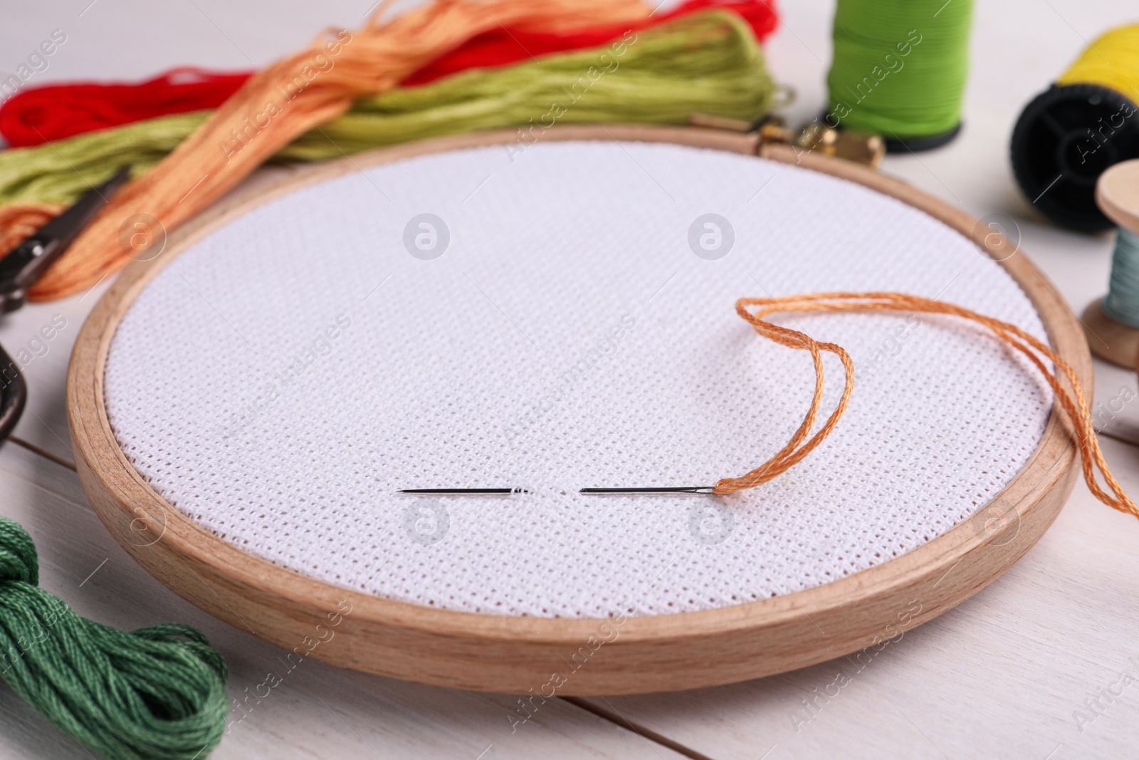 Photo of Embroidery hoop with fabric and needle on white wooden table, closeup