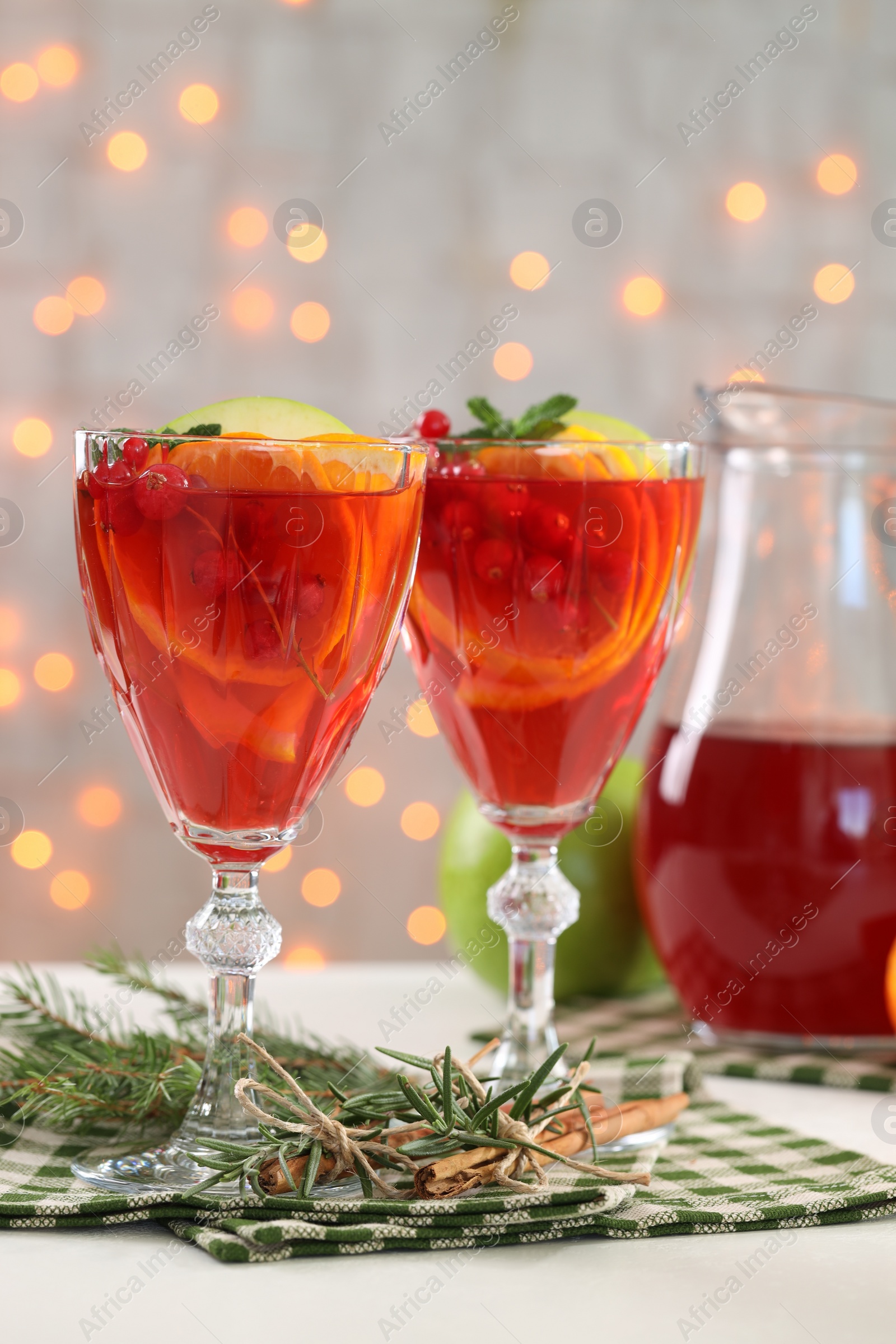 Photo of Christmas Sangria cocktail in glasses, cinnamon sticks and fir tree branch on white table against blurred lights