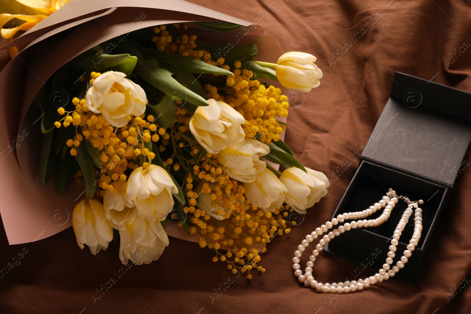 Photo of Bouquet of beautiful spring flowers and necklace on brown fabric, above view