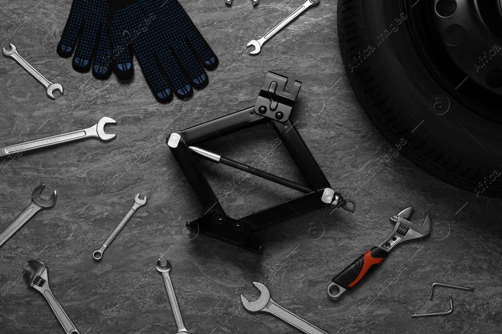 Photo of Car wheel, scissor jack, gloves and different tools on grey stone surface, flat lay