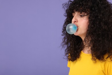 Photo of Beautiful young woman blowing bubble gum on purple background. Space for text