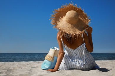 Photo of Woman with beach bag and straw hat lying on sand near sea, back view