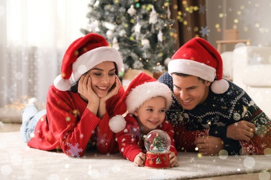 Image of Family in Santa hats playing with snow globe at home