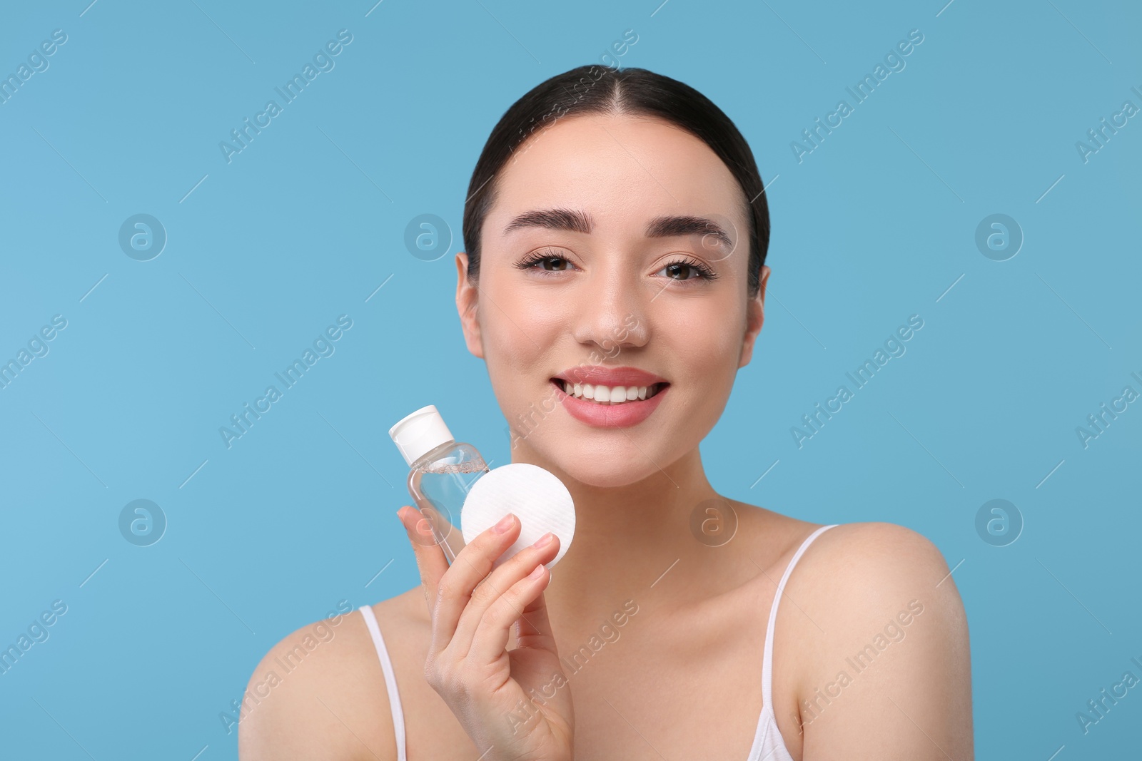 Photo of Beautiful woman with makeup remover and cotton pad on light blue background