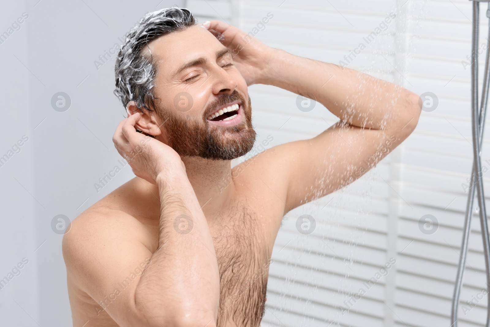 Photo of Happy man washing his hair with shampoo in shower