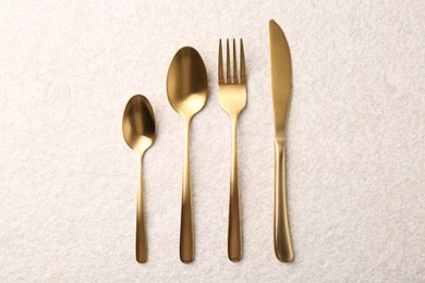 Photo of Stylish golden cutlery set on light textured table, flat lay
