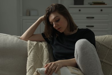 Photo of Sad young woman sitting on sofa at home