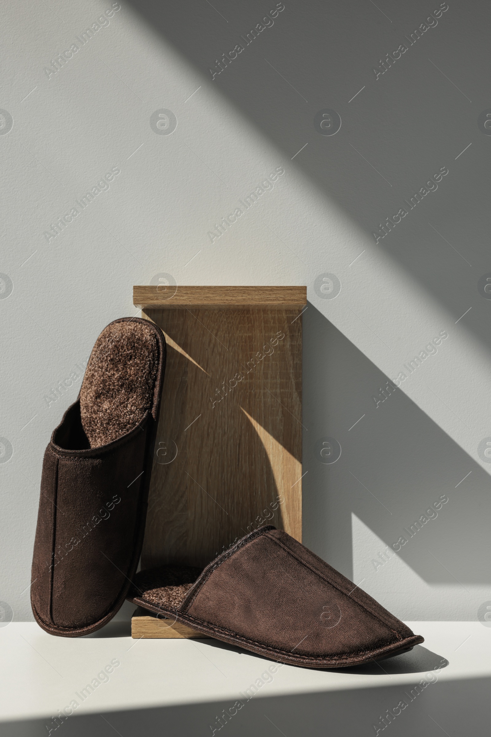 Photo of Pair of brown slippers and wooden stand on floor