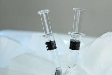 Syringes with COVID-19 vaccine on ice cubes, closeup