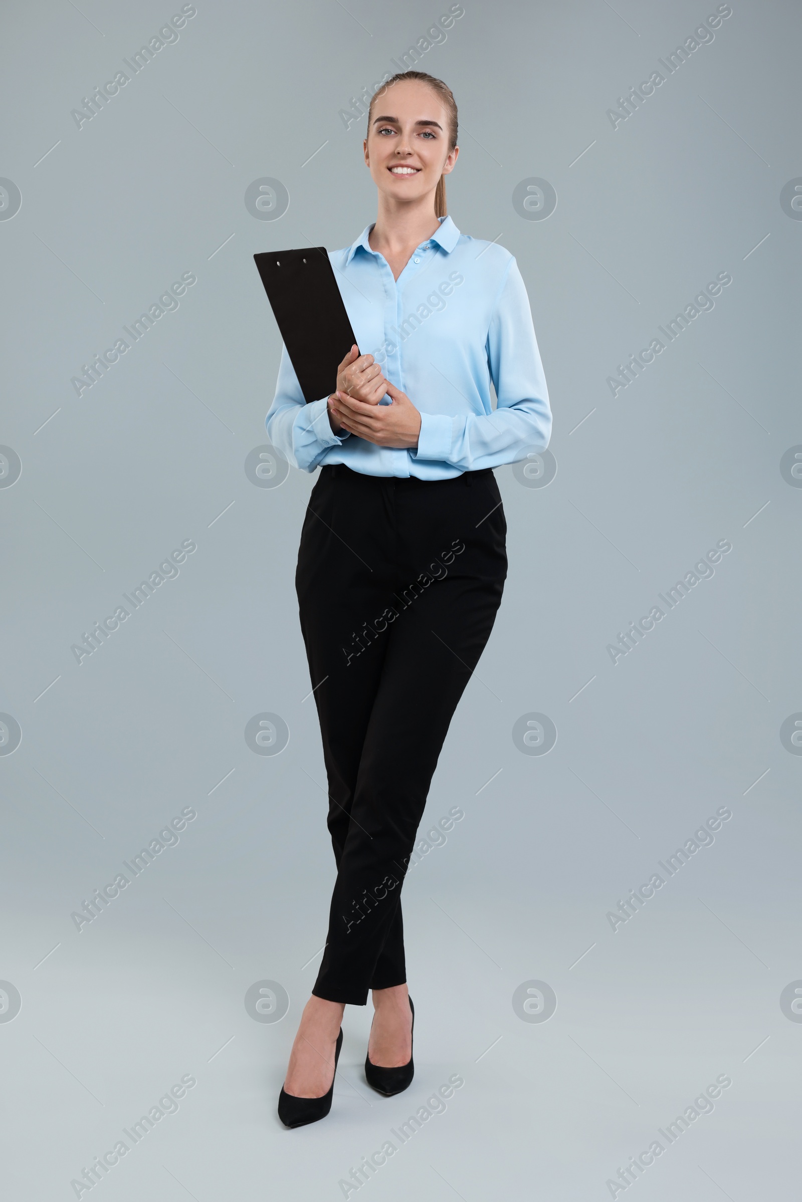 Photo of Happy young secretary with clipboard on grey background