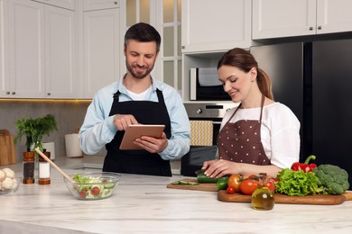 Photo of Happy couple reading recipe on tablet while cooking in kitchen. Online culinary book