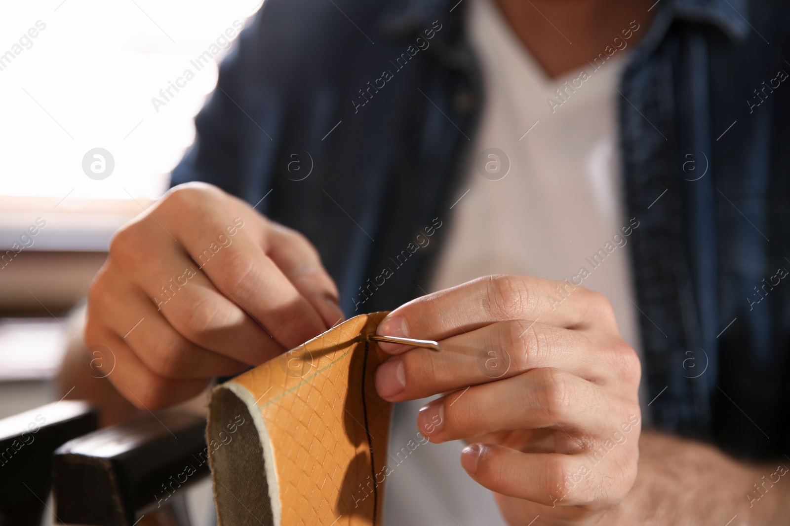 Photo of Man sewing piece of leather in workshop, closeup