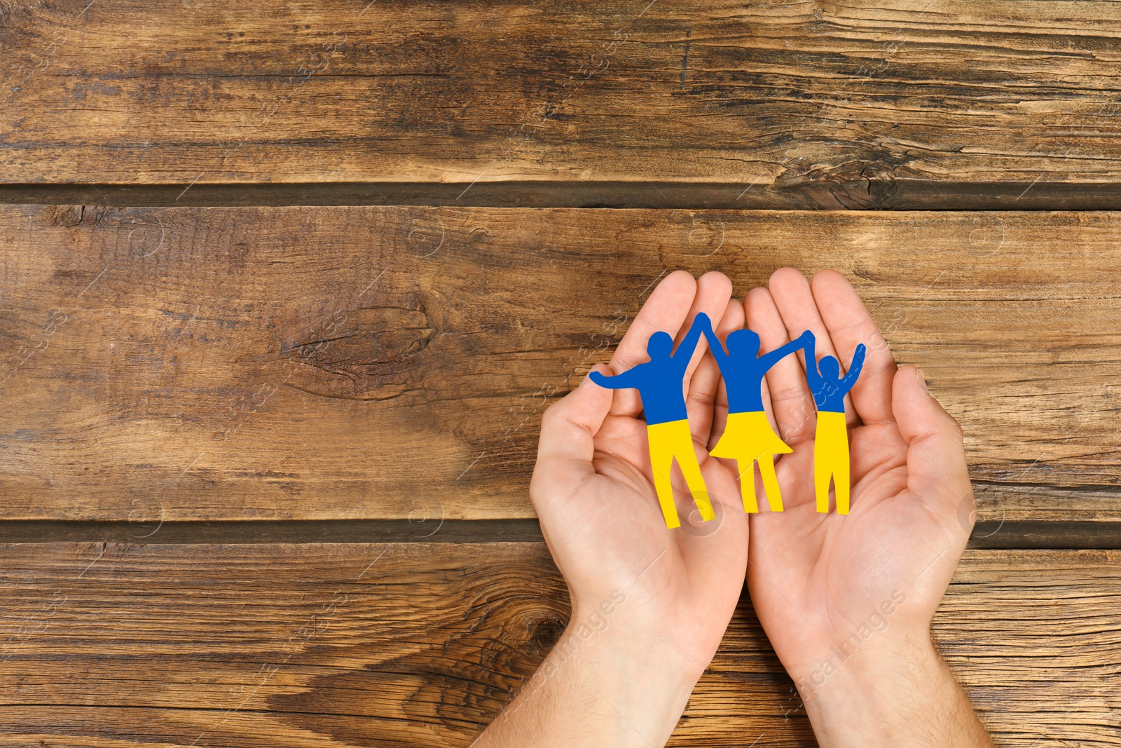 Image of Man with paper family figure in colors of Ukrainian flag at wooden table, top view. Space for text