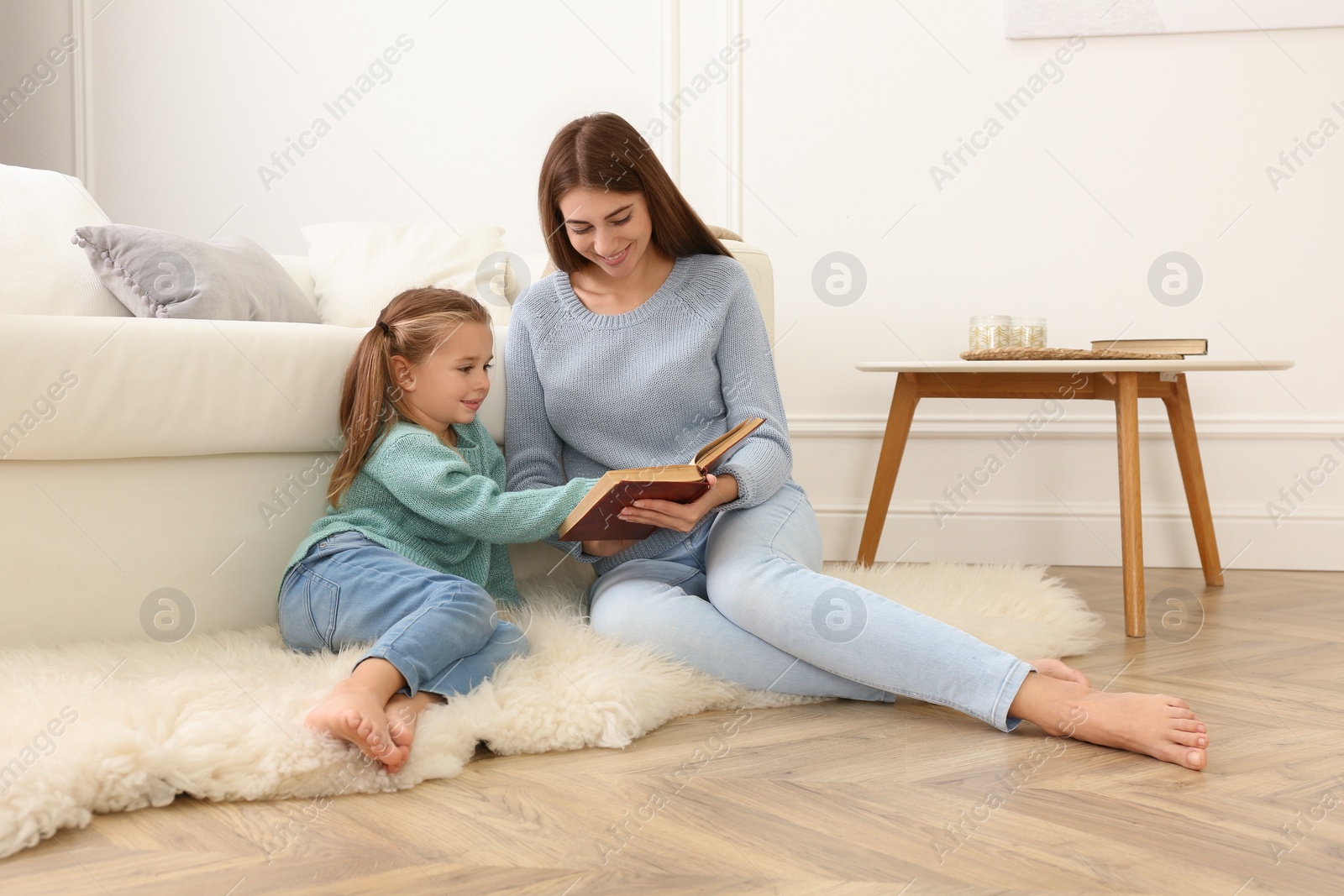 Photo of Mother and her daughter reading book at home. Floor heating concept