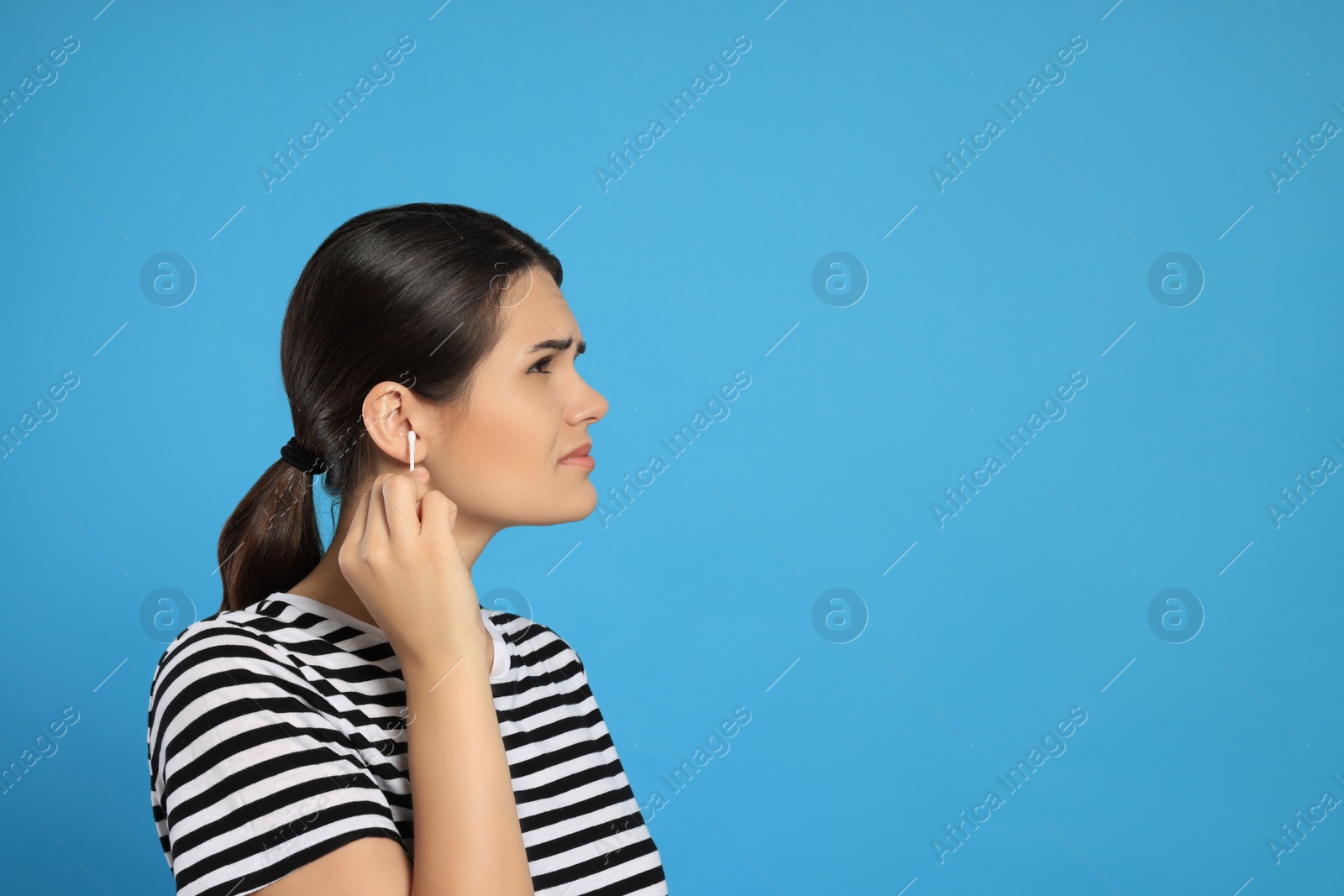 Photo of Young woman cleaning ear with cotton swab on light blue background, space for text